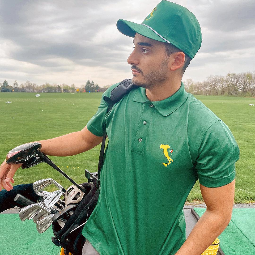 Man wearing green Italian boot polo shirt and green hat, carrying golf clubs. 